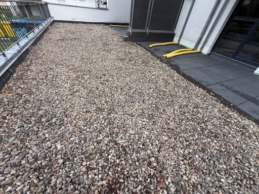 Grau-weiße Kiesfläche auf einem Balkon, neben einem Gebäude.